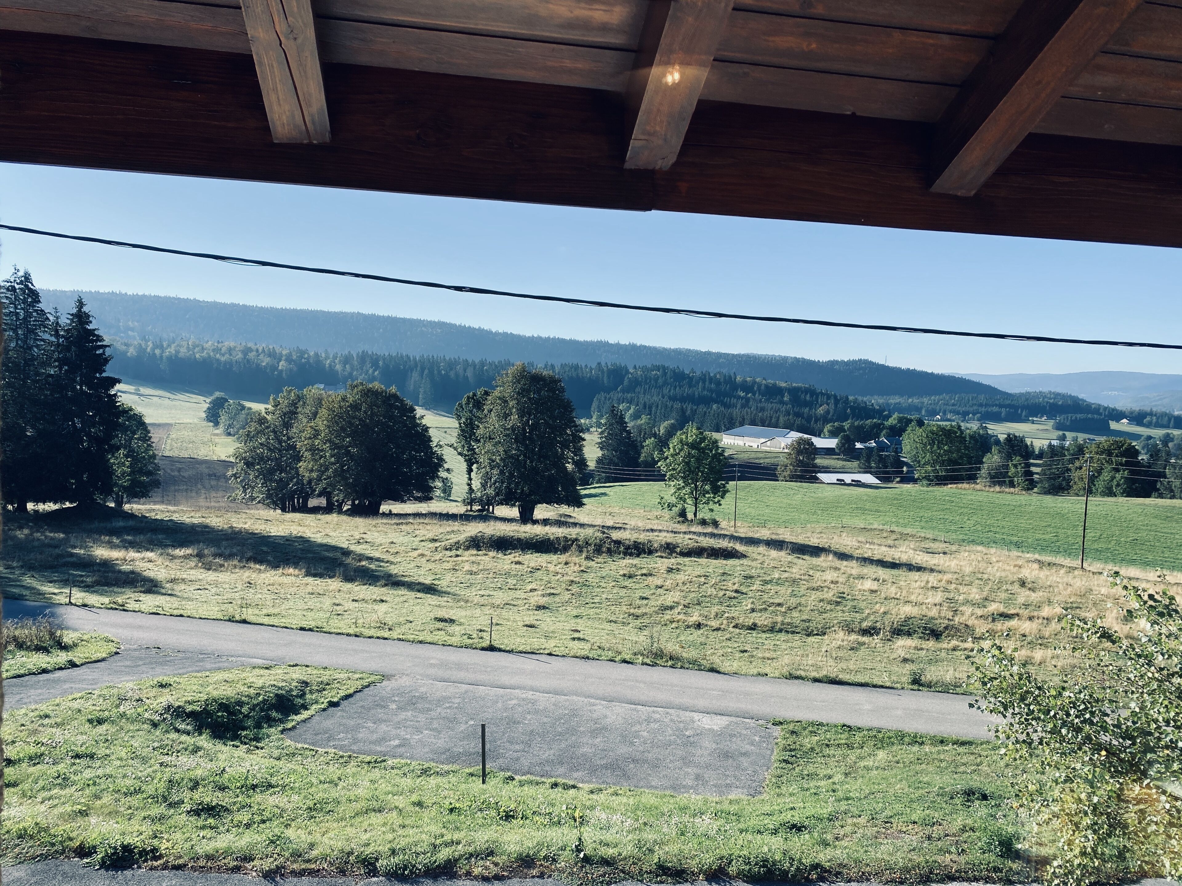 Une vue depuis un porche abrité, donnant sur un paysage rural avec des arbres, une route et des bâtiments situés au loin.