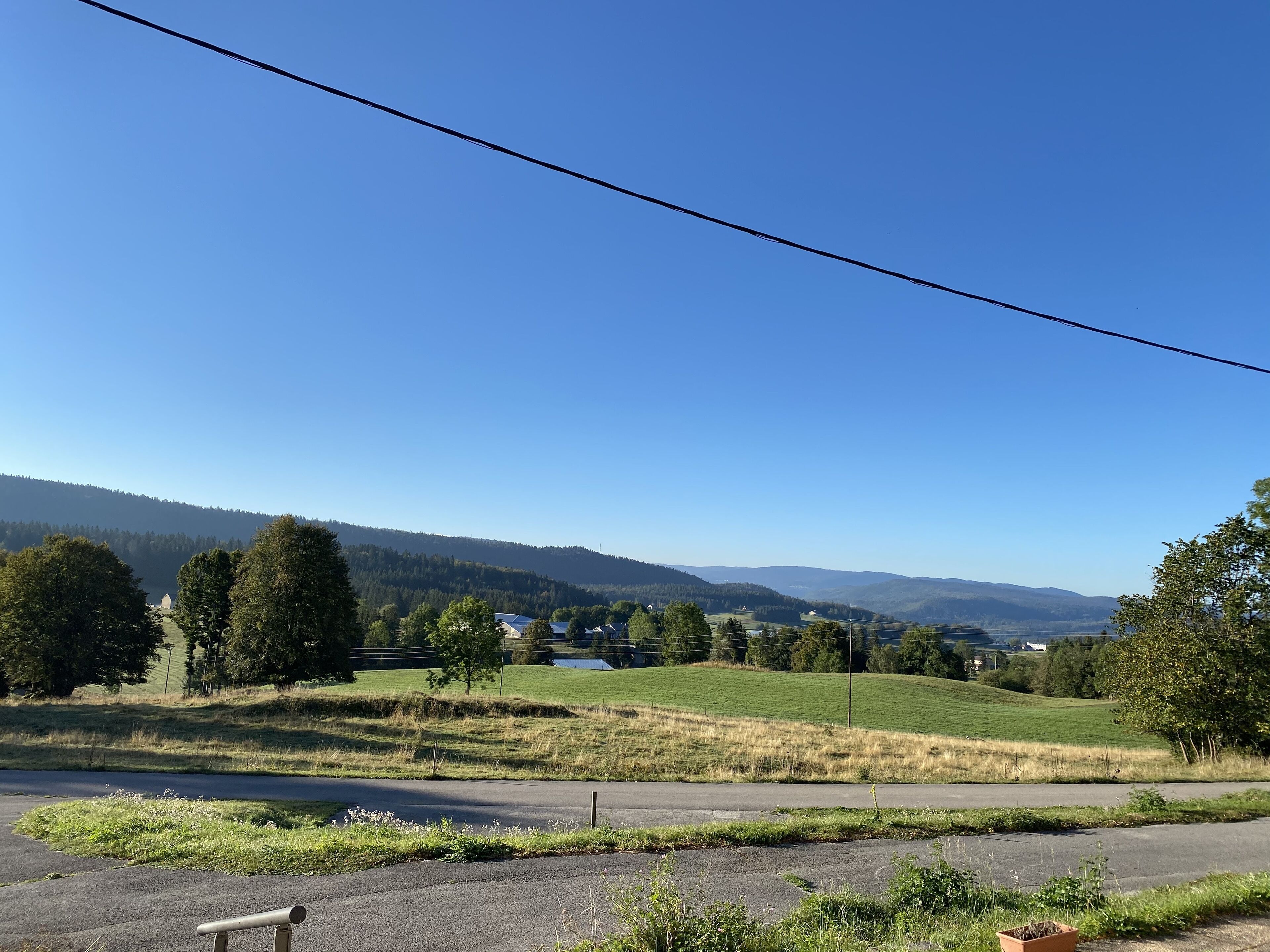 A rural landscape with a road, green fields, and distant hills.