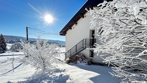 Een besneeuwd landschap met een huis met balkon en uitzicht op een besneeuwd berglandschap.
