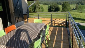 Een balkon met een tafel en stoelen, met uitzicht op een groen landschap en een bebost gebied.