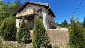 A modern house with a wooden balcony, surrounded by evergreen trees. - GITE 2 to 5 PERS HAUT JURA PLEINE NATURE (Morbier)