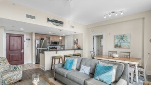 A modern living room with a grey sofa, a coffee table, and a dining area with a wooden table and chairs. - Full Kitchen ~ Private Balcony ~ Resort Pool (Miramar Beach)