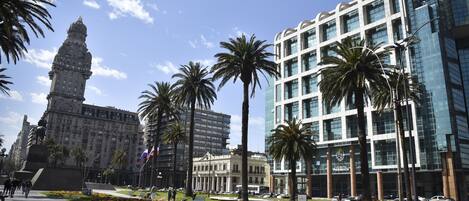 A cityscape with a historic building, modern skyscrapers, palm trees, and a clear sky.