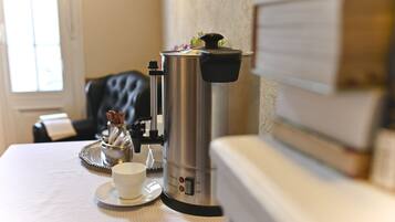 A coffee maker on a table with a cup and saucer, a tray, and a decorative item.