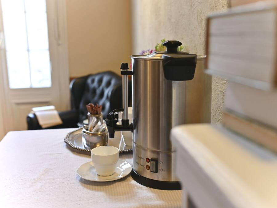 A coffee maker on a table with a cup and saucer, a tray, and a decorative item.