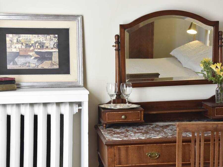 Un dormitorio con un aparador de madera, un espejo, un cuadro enmarco y un florero con flores.