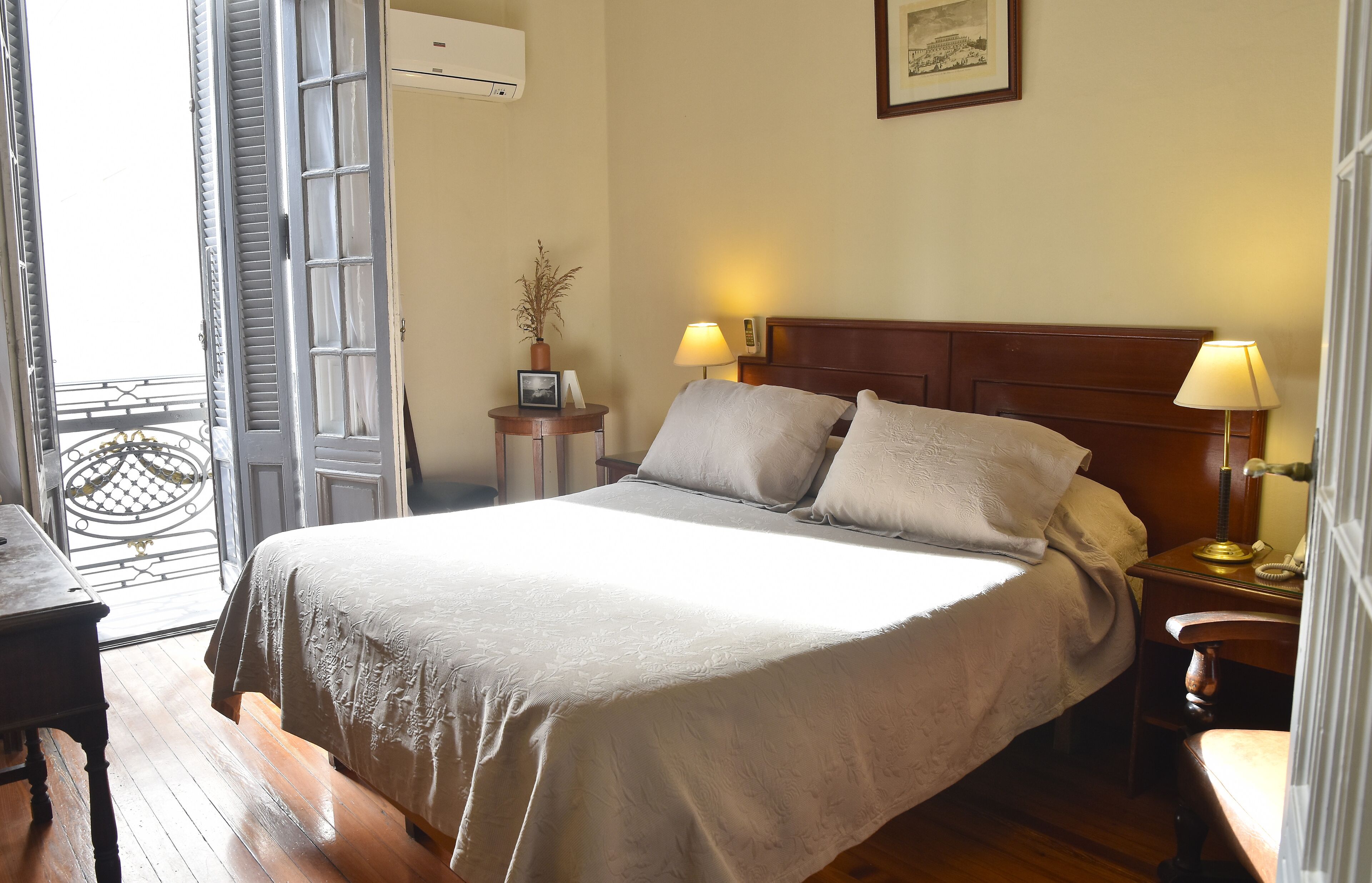 A neatly made bed with a wooden headboard, two bedside lamps, and a small table with a lamp and a picture frame.
