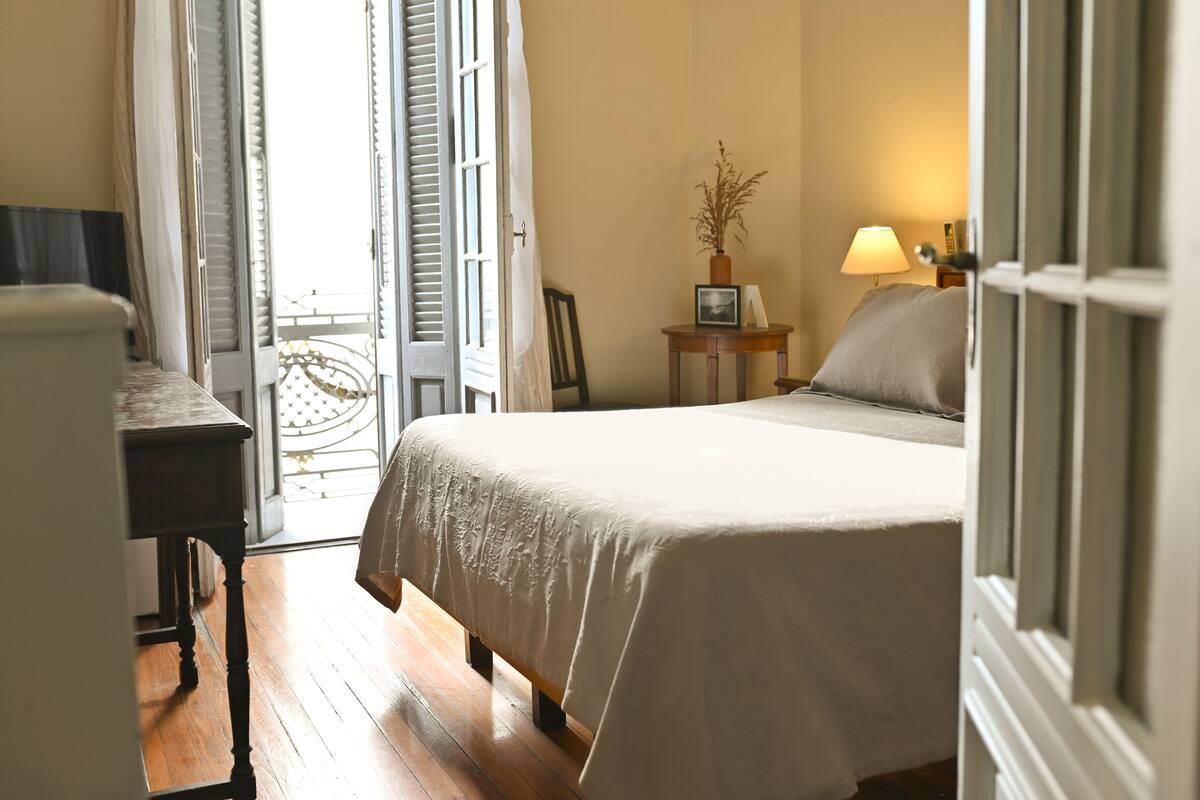 A bedroom with a bed, a bedside table, a lamp, and a window with curtains.