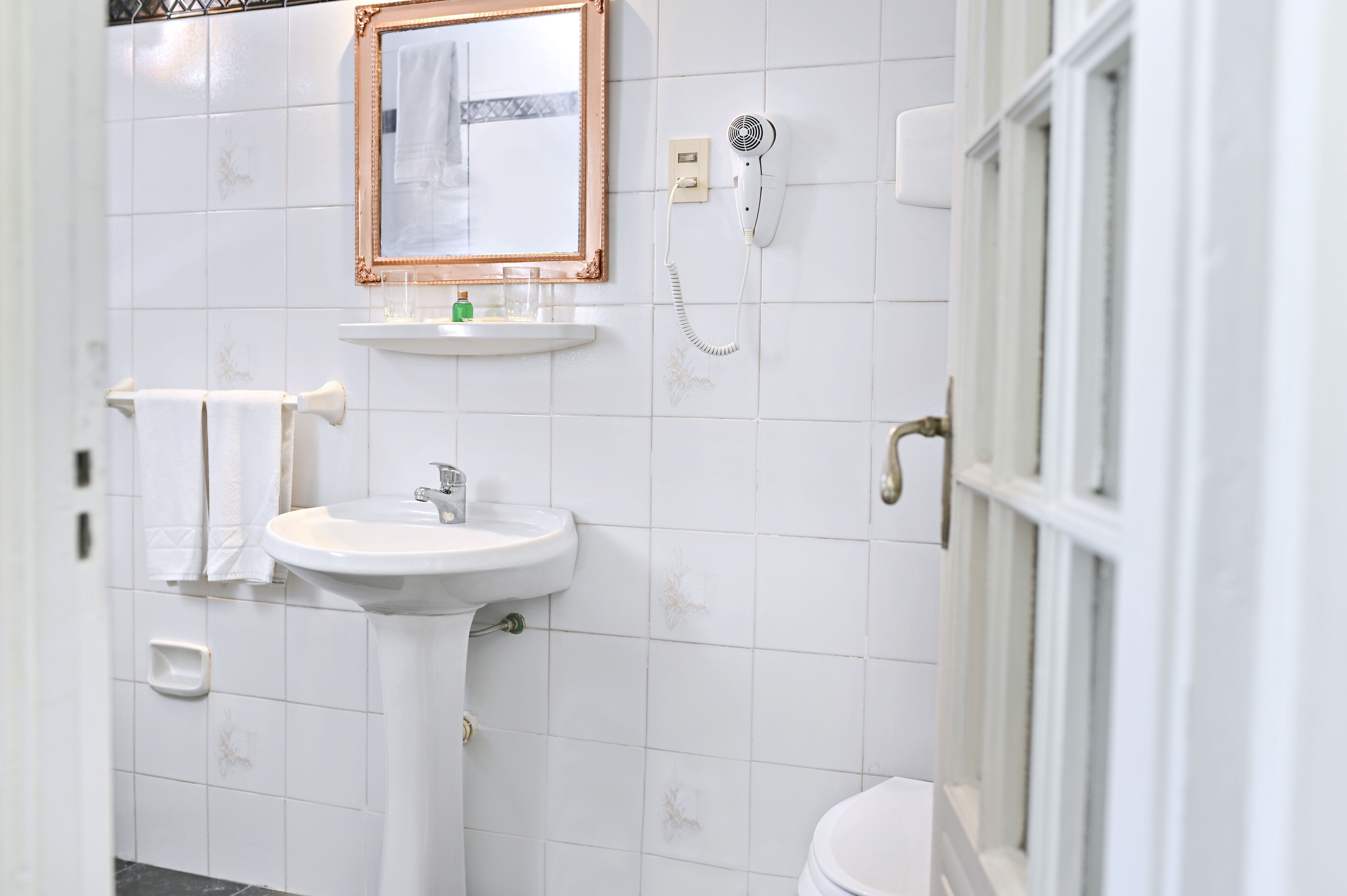 A bathroom with a white sink, a mirror, a hairdryer, and a toilet.