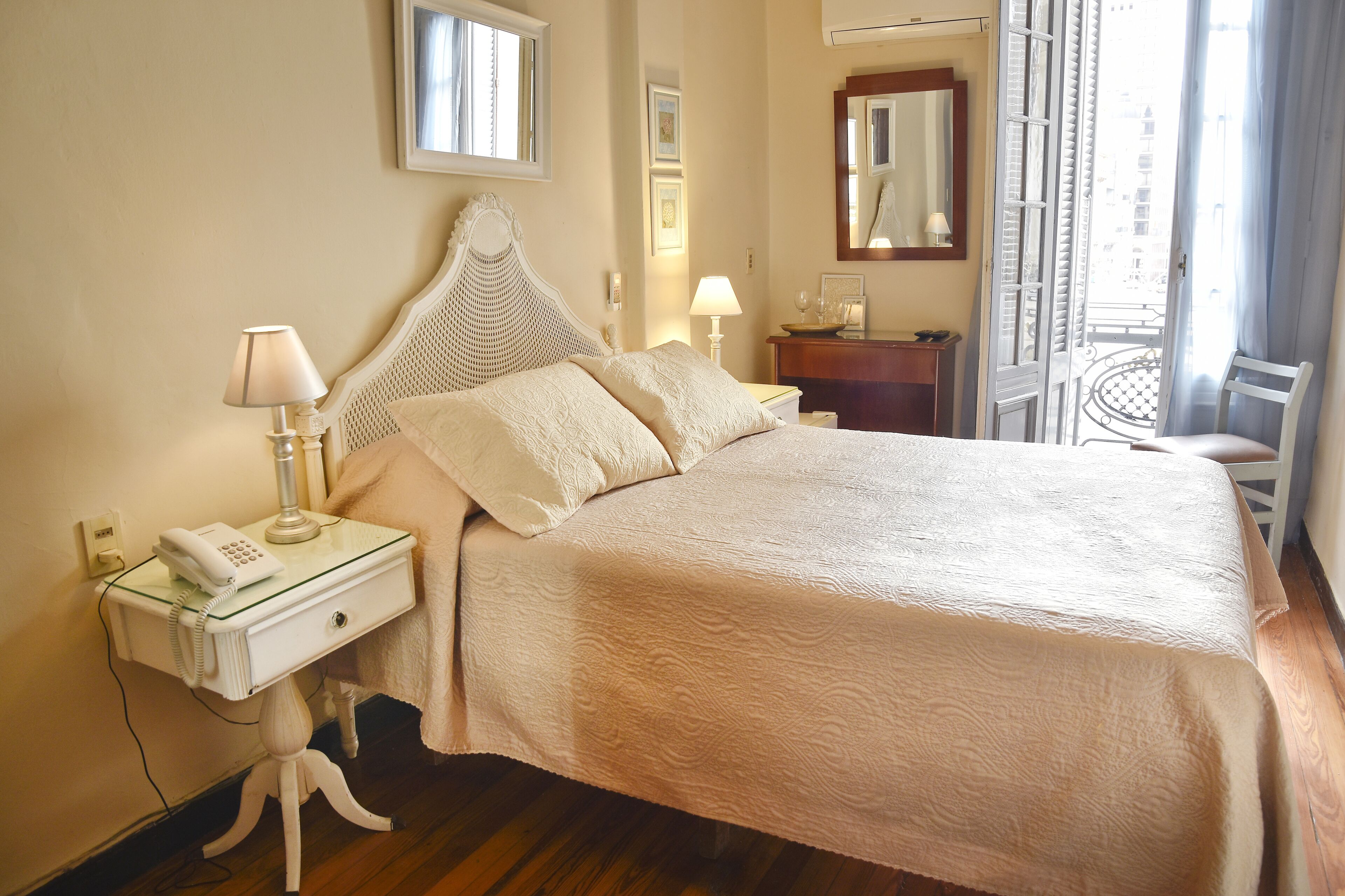 A neatly made bed with a white headboard, a bedside lamp, and a telephone on a glass-topped nightstand.