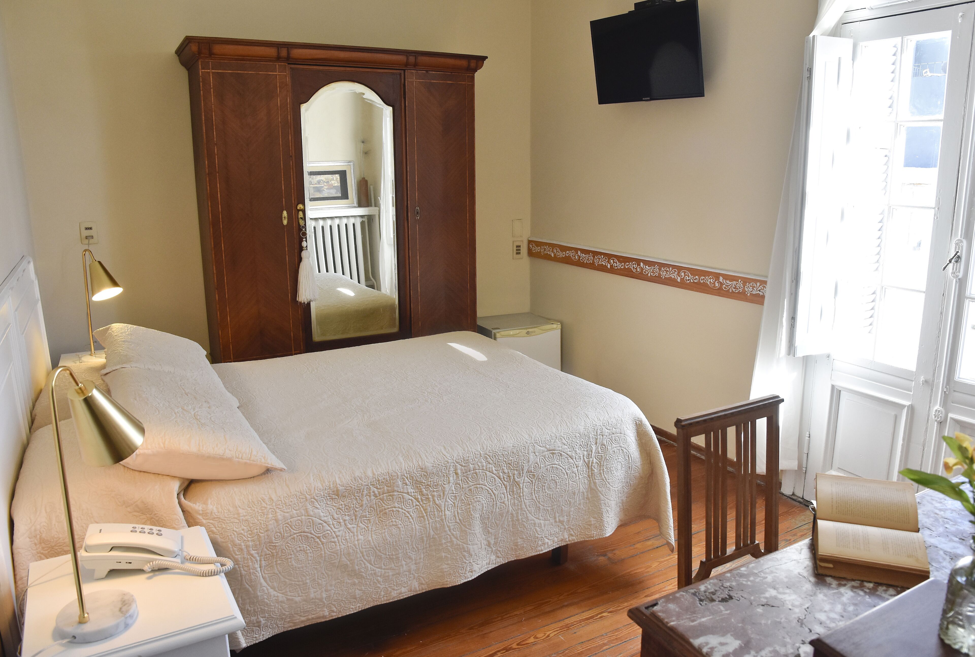 A bedroom with a bed, bedside lamp, telephone, and a wooden wardrobe.