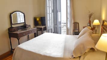 Un dormitorio con cama, cómoda, televisor y ventana con contraventanas.