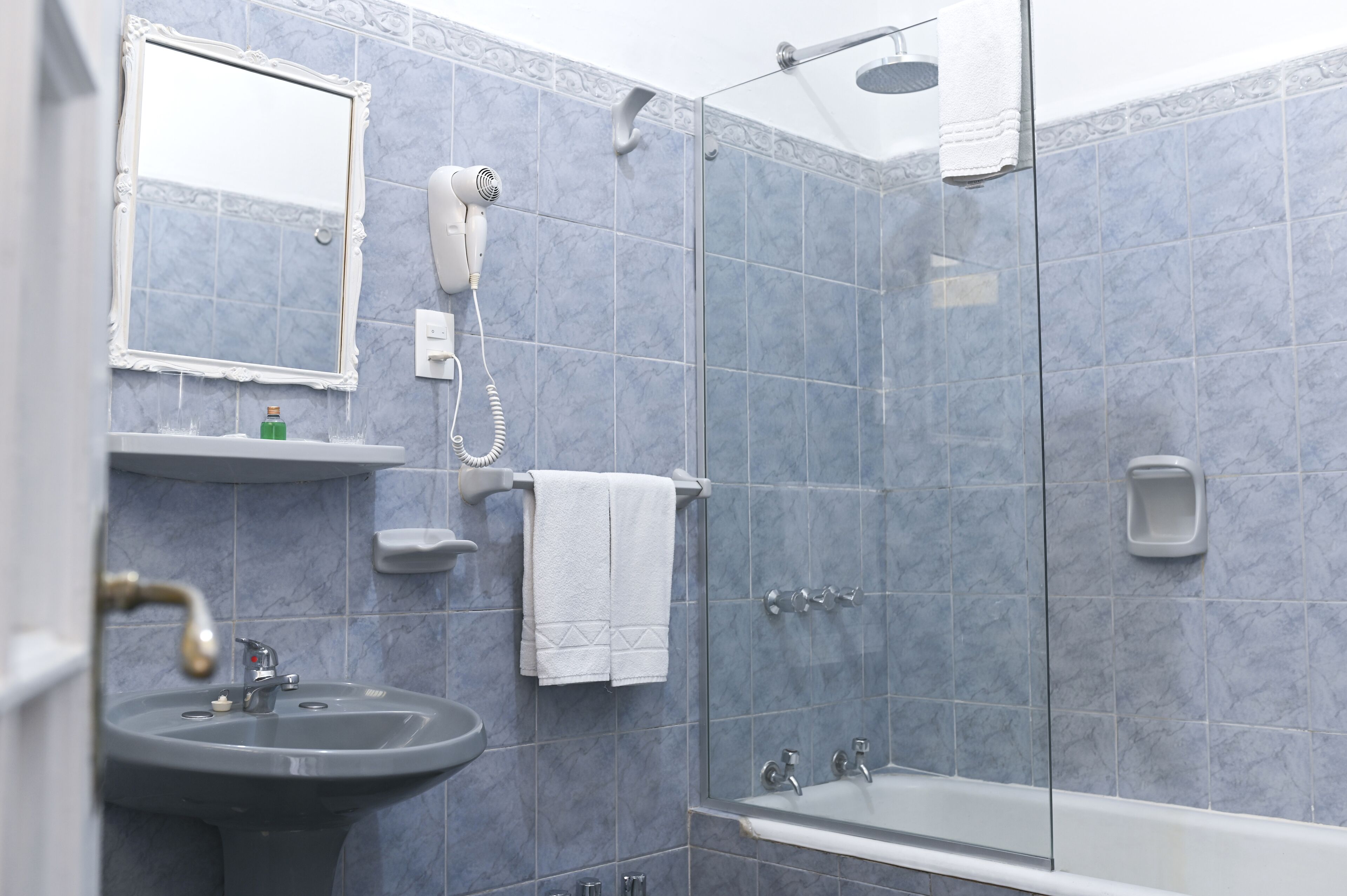 A bathroom with a sink, mirror, hairdryer, and shower.