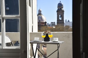 Un balcón con una mesa lista para dos personas, con un jarrón de flores y dos vasos de jugo de naranja.