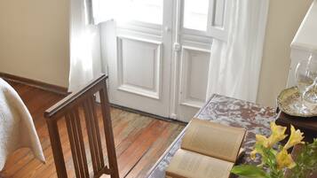 Ein Holzhocker, ein Tisch mit einem Buch, eine Vase mit Blumen und ein Fenster mit Vorhängen.