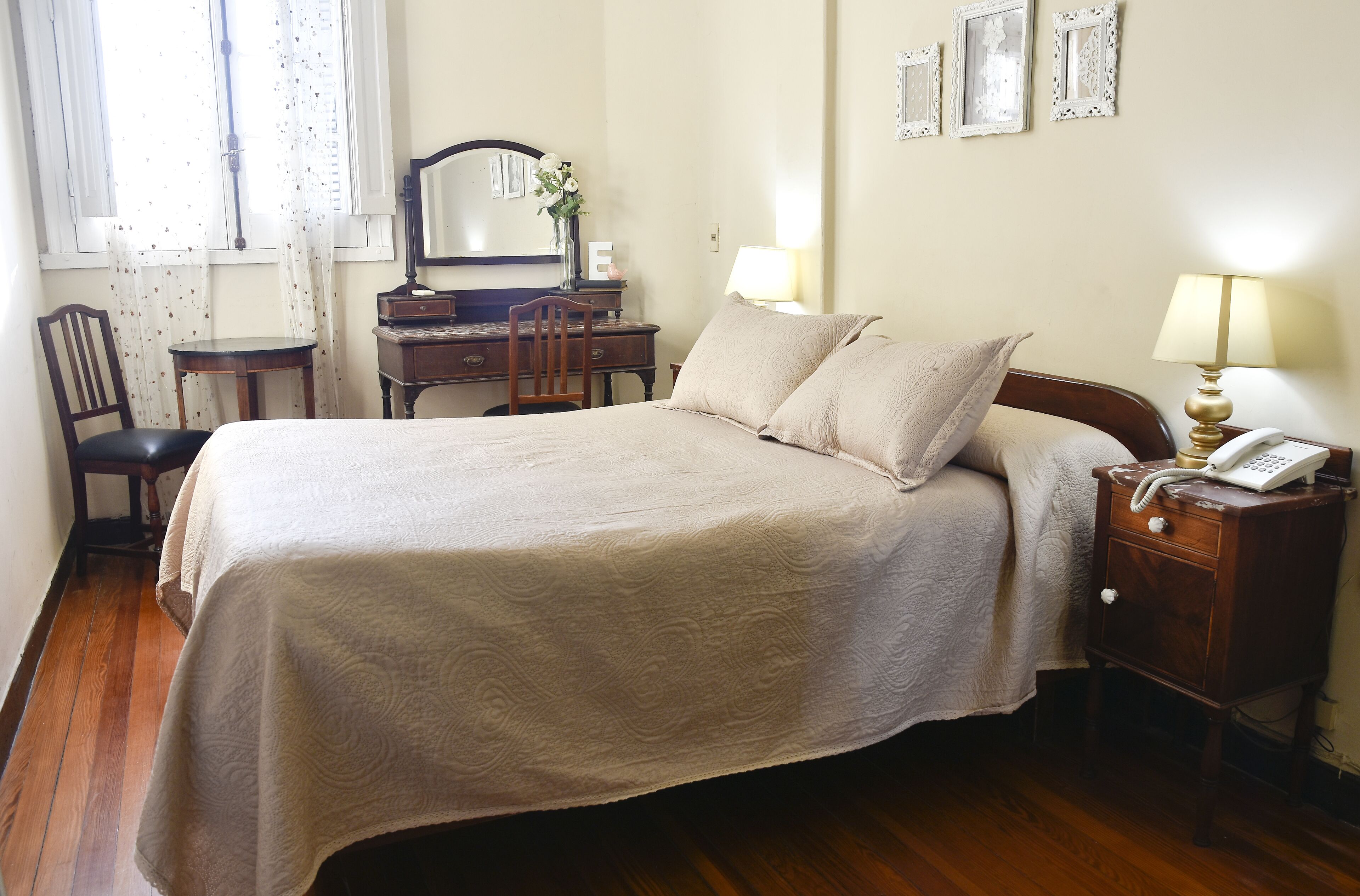 Une chambre bien rangée, avec un lit, une table de chevet, une lampe et une commode dotée d’un miroir.