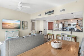 A modern kitchen with a central island, wooden dining table, and bar stools. - Bayside Resort ~ Spacious Balcony ~ Resort Pool (Miramar Beach)