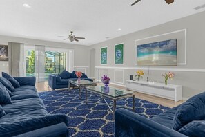 A modern living room with a blue sofa set, a glass coffee table, and a white entertainment unit. - Multiple Themed Rooms • Theater • Pool & Spa • Waterslides • Gated Resort (Davenport)