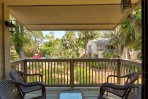 A covered porch with wicker furniture, a view of a residential area, and a house with a balcony.