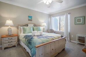 A bedroom with a bed, two bedside tables, a nightstand, a ceiling fan, a window with blinds, and a wall clock.
