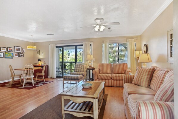 A living room with a dining area, a ceiling fan, and a view through a glass door.