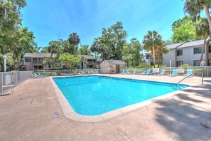 Una piscina rectangular con agua azul cristalina, rodeada de sillas de descanso y palmeras.