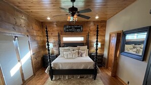 A bedroom with a four-poster bed, wooden walls, a ceiling fan, and a framed mirror on the wall. - Lodge on The Lake (Rutledge)