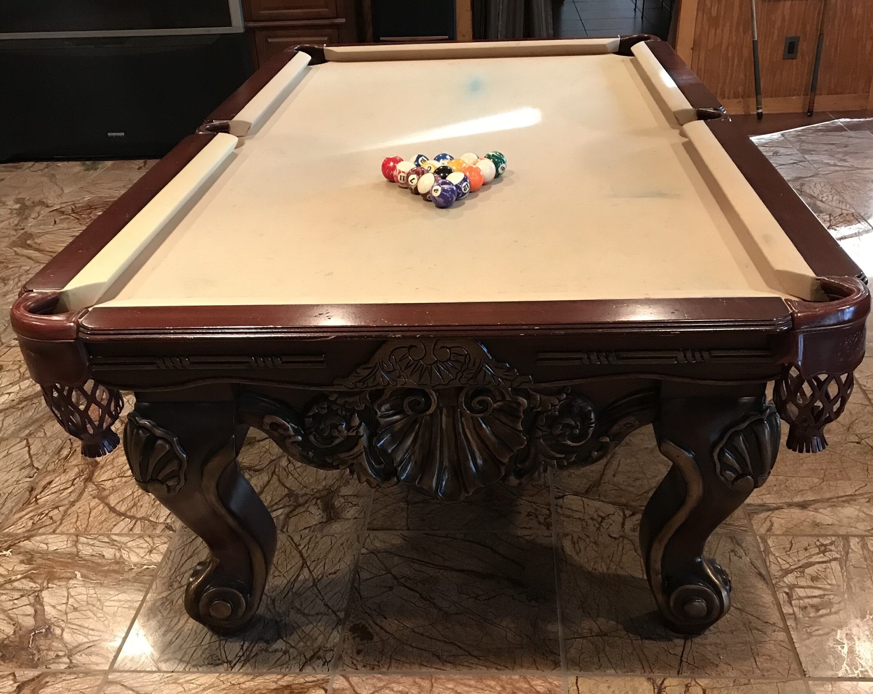 A pool table with a wooden frame and ornate carvings, positioned on a marble floor.