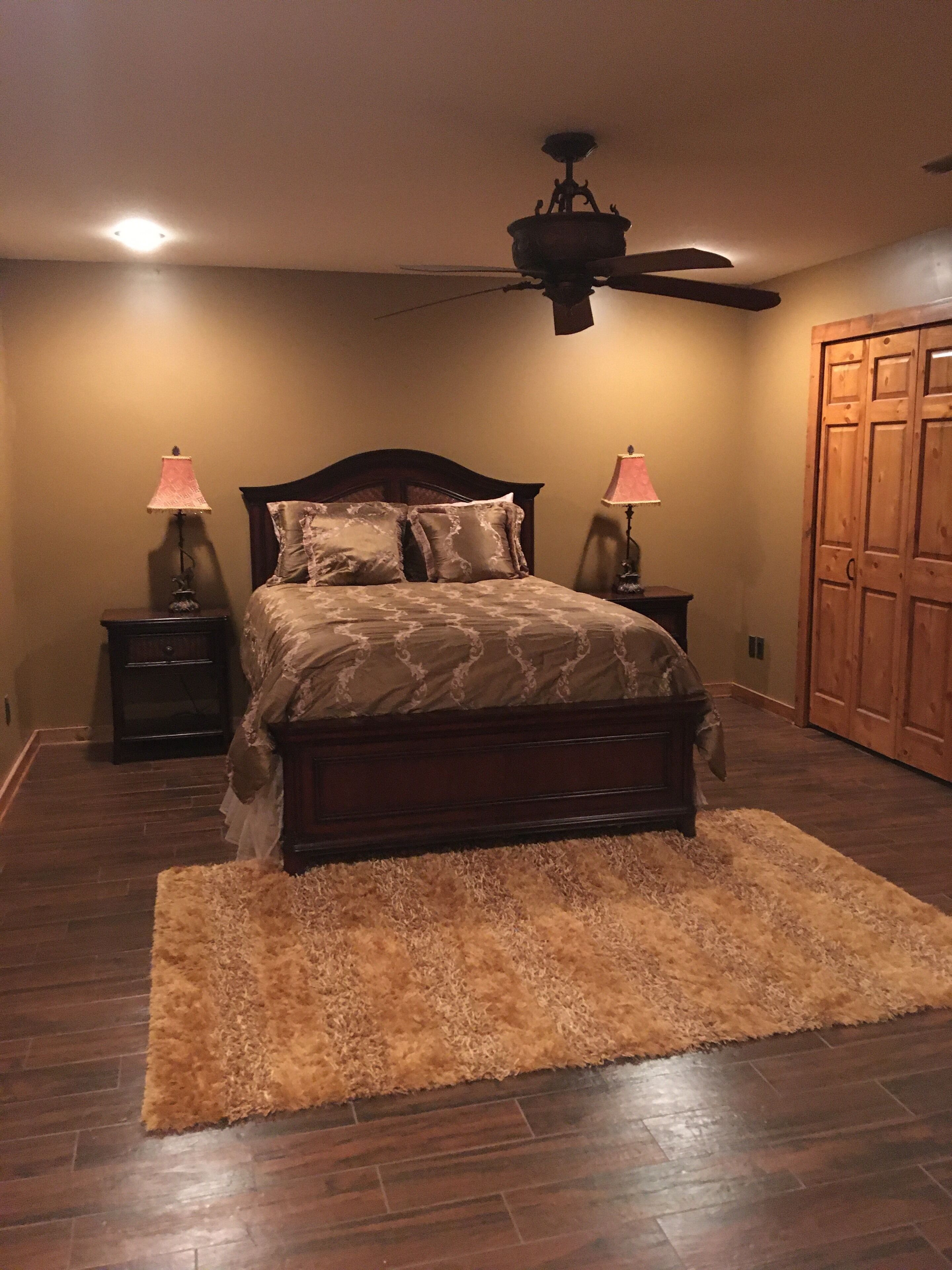 A bedroom with a bed, two bedside tables with lamps, a ceiling fan, a wooden wardrobe, and a fluffy rug.