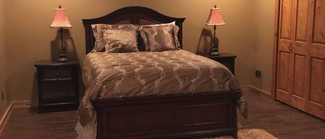 A bedroom with a bed, two bedside tables with lamps, a ceiling fan, a wooden wardrobe, and a fluffy rug.