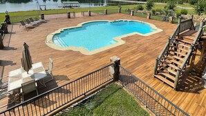 A wooden deck with a swimming pool, outdoor seating, and a view of a lake and trees. - Lodge on The Lake (Rutledge)