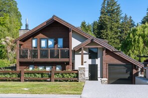 A two-story wooden house with a garage, a balcony, and a stone foundation. - Mountain View Chalet (Wanaka)