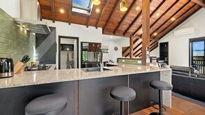 Une cuisine moderne dotée d’un plan de travail en granit, d’appareils électroménagers en acier inoxydable et d’un plafond en bois.
