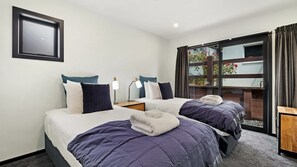 A hotel room with two beds, a bedside table with a lamp, a window with curtains, and a framed picture on the wall. - Mountain View Chalet (Wanaka)