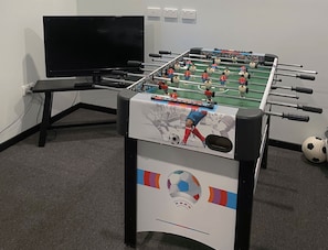 A foosball table with a soccer ball and a television in the background.