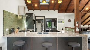 A modern kitchen with a central island, bar stools, and a view into the living area. - Mountain View Chalet (Wanaka)