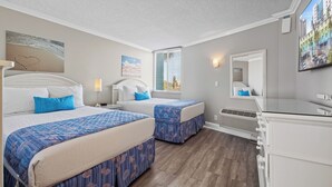 Habitación de hotel con dos camas, una ventana con persianas, un espejo, un calentador y un televisor montado en la pared.