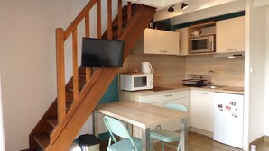 A compact kitchen with a wooden staircase, a microwave, a kettle, and a small dining table with chairs.