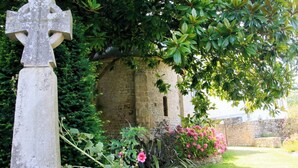 A stone cross in a garden with a stone wall and flowering plants.