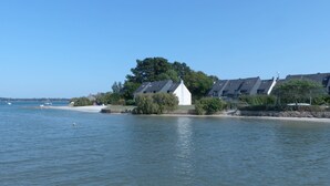 A lakeside view with a row of modern houses, a small white structure, and a sandy beach.
