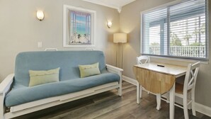 A room with a blue sofa, a wooden table, and a window with blinds. - Pelican Pointe 227:Walk to Beach~Pool~Free Parking (Clearwater)