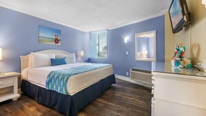 Ein Schlafzimmer mit einem Bett, Nachttischen, einer Kommode, einem Fernseher, einem Fenster mit Jalousien und einem Bild an der Wand.