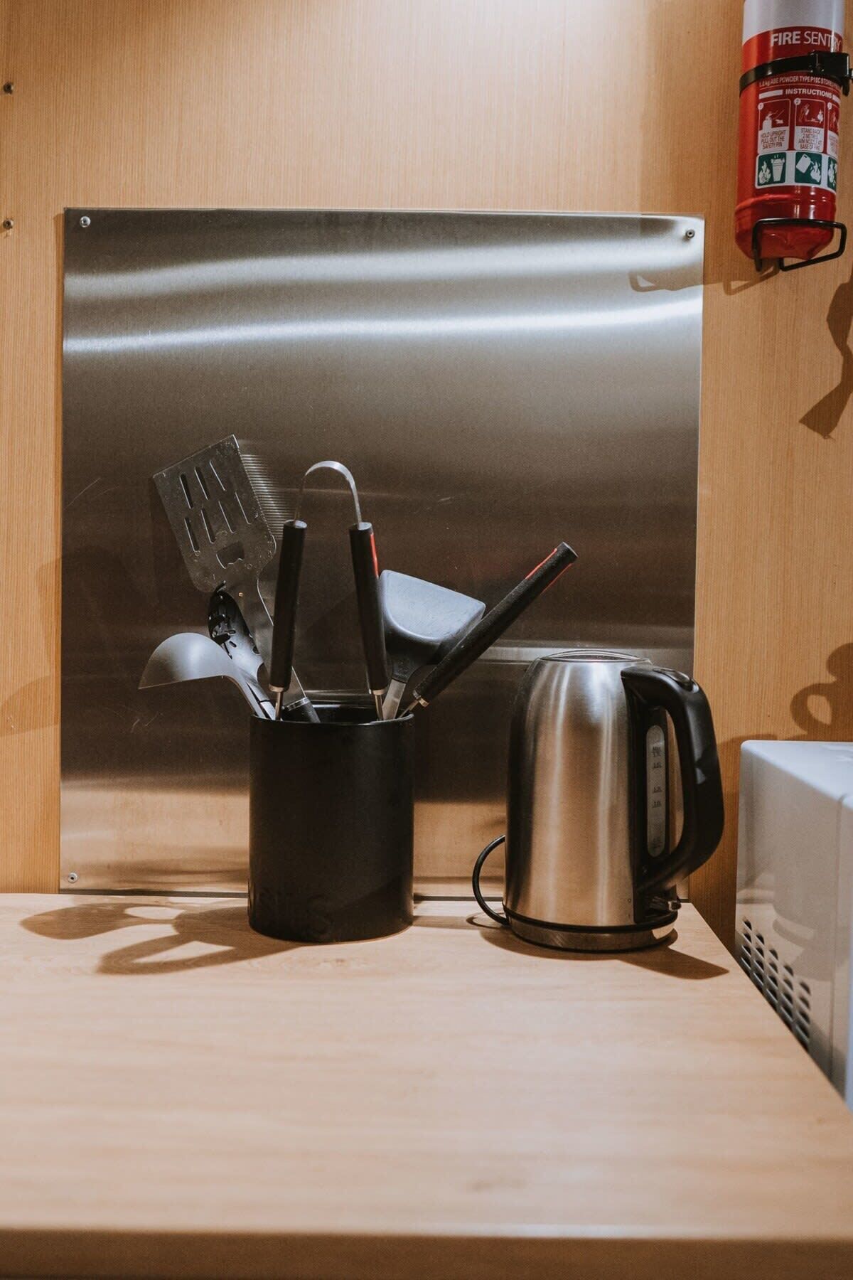 Une bouilloire en acier inoxydable et une casserole noire avec des ustensiles, le tout posé sur une étagère en bois.