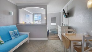 A compact living space with a blue sofa, a wooden dining table, and a TV mounted on the wall.