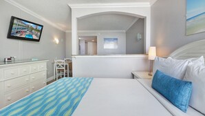 A hotel room with a bed, a desk, a chair, a television, and a window with a view of a building.