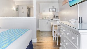 Habitación de hotel compacta con cama, kitchenette, un pequeño comedor y televisor montado en la pared.