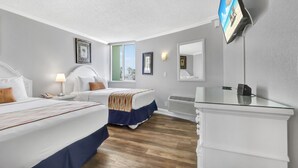 A hotel room with two beds, a TV, a mirror, and a window with blinds.