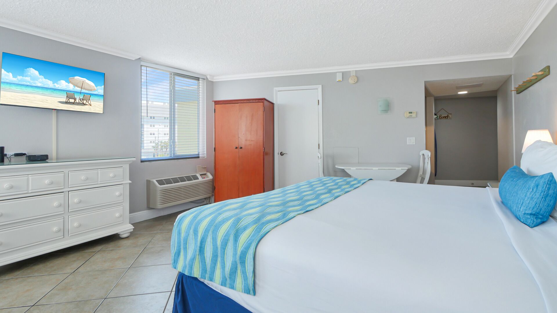 A bedroom with a bed, dresser, and a painting of a beach scene.