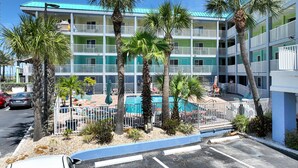 Un hotel de varios pisos con piscina, palmeras y estacionamiento.
