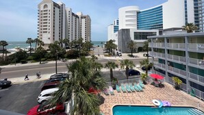 Un hotel con zona de piscina, que incluye sillas de descanso y sombrillas, con vistas a una playa con palmeras y un cielo despejado.